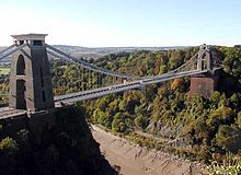 A suspension bridge spanning a river gorge with woodland in the background