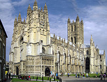 Large yellow stone ornate building with buttresses and square central tower.