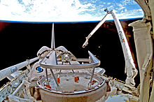 A shuttle in space, with Earth in the background. A mechanical arm labeled 