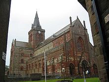 A large church made from red and yellow stone with a square tower and a spire on the tower.