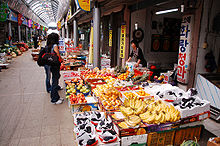 A female customer browsing a fruit shop. Banana and grapes are displayed on the front.