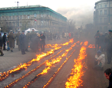 A number of candles are arranged in a cross shape in a roadway, while a crowd of people look on.