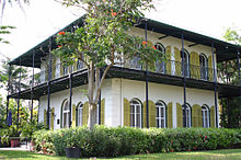 two story square house with tall windows and exterior shutters and a second story porch